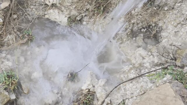 Clear water falling and splashing down in a natural outdoor setting, droplets captured in motion as water pours downward, bright sunlight reflecting on the falling water creating sparkling effects, fr
