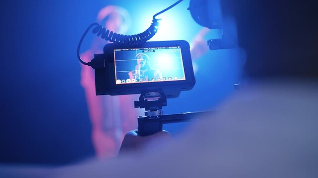 Professional filmmaker operating a camera, shooting a singer performing on a smoky stage with blue and pink lights for a music video production