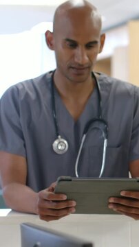 Vertical video: Pullback showing Dr in scrubs with steth tapping tablet at counter checking chart