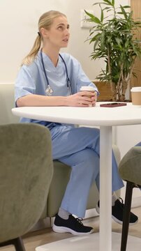 Vertical video: Holding cup, clinician in scrubs chatting in lounge on break as peer placing cup