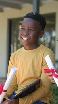Vertical video: Handing red ribbon cert causing boy in mustard shirt with folder at school smiling