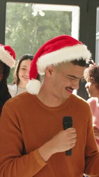Vertical video: Cueing man in Santa hat rust sweater singing for group at home, holding mic, drink