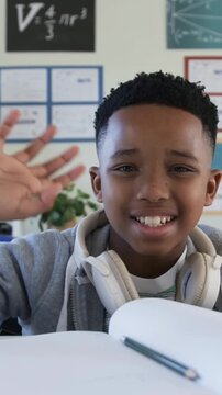 Vertical video: Clip opening boy greeting camera taking pencil writing notebook in classroom hoodie