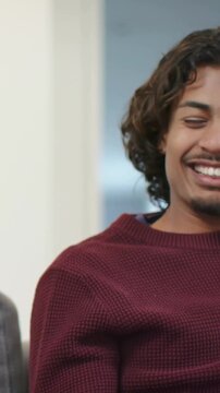 Vertical video: Shot widening man in maroon knit smiling and checking phone on gray couch, reacting