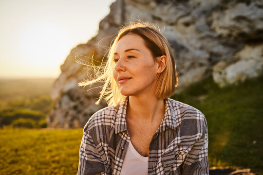 Young Woman Gazing Into Distance at Sunset Near Rocky Hillside With Wind in Hair