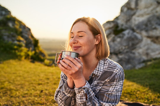 Young Woman Savoring Hot Drink from Metal Cup During Sunset Hike in Rocky Mountains