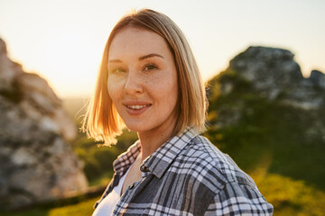Young Woman with Freckles Smiling Outdoors During Golden Hour in Rocky Landscape