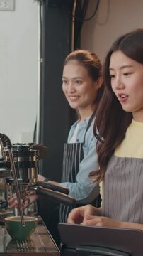 Vertical Screen : Young Asia female use mobile phone pay contactless with tablet at cafe restaurant. Girl barista talk receive orders from customer at bar counter in coffee shop. Owner small business.