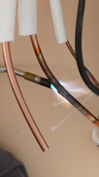 Professional hvac technician using a blowtorch to solder copper pipes while installing a new air conditioning system, joining the metal tubes with a strong, permanent connection