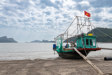 Fishing boat with vietnam flag resting on the low tide beach in hi phong