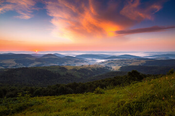Fototapeta premium Gorgeous sunrise illuminates the rolling hills and misty valleys of a serene mountain landscape in early morning light.