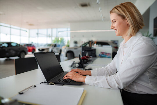 Woman sales manager working on laptop in car dealership