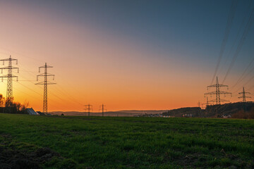 Naklejka premium A scenic sunset over a green field with high voltage power lines in the rural landscape of germany.