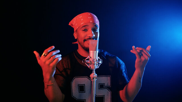 Male singer performing a rap song in a music studio, mic ready for recording, cool neon lighting creating a dynamic atmosphere