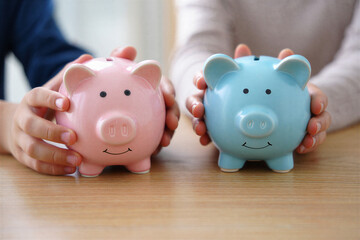 Two piggy banks pink and blue held by hands saving