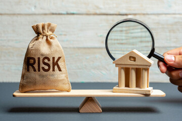 Burlap sack labeled risk on seesaw with wooden building