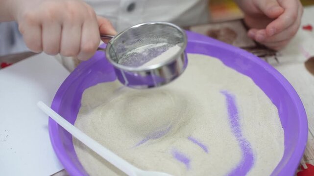 A child at a master class sifts sand through a sieve in close-up. High quality video