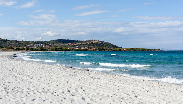 Sandy beach along Sardinia coastline. Turquoise sea waves by the shore. S'Ena e Sa Chitta view in the distance. Clear sky above the scenic landscape.
