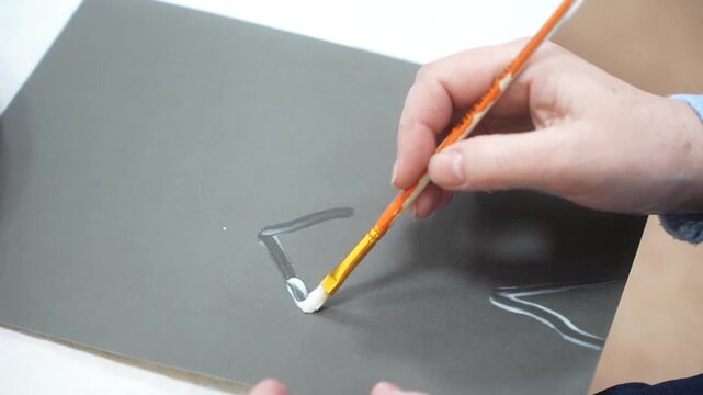 The child and the mother paint the paper with glue to fill the drawing with sand. Developing master class