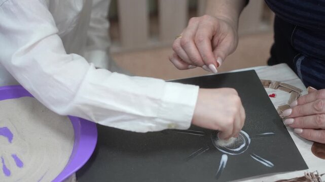 The child and the mother paint the paper with glue to fill the drawing with sand. Developing master class
