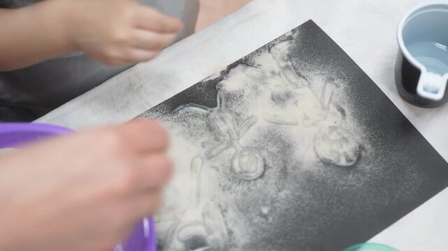The child and the mother paint the paper with glue to fill the drawing with sand. Developing master class