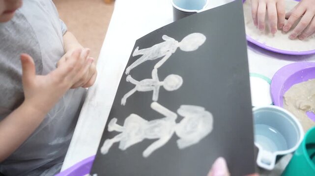 The child and the mother paint the paper with glue to fill the drawing with sand. Developing master class