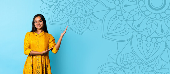 A woman stands on a blue background showing a design. She is smiling and has her arm extended. The background features a decorative pattern. This moment captures a creative and bright activity. © Prostock-studio