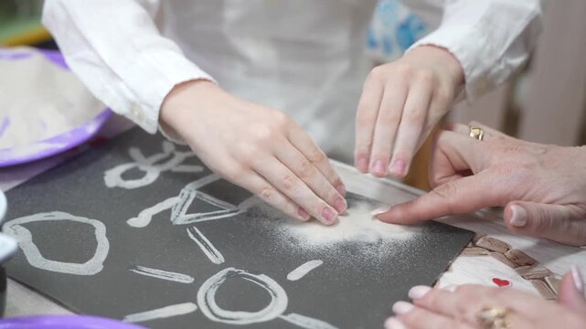 The child and the mother paint the paper with glue to fill the drawing with sand. Developing master class