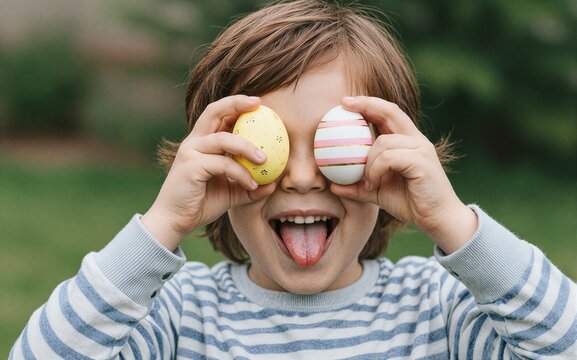 Child holds colorful eggs over eyes tongue out in playful Easter pose.