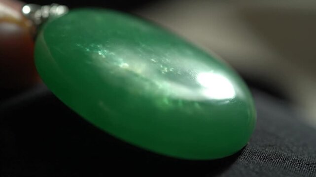 Close-up of a vibrant green jade pendant, showcasing its smooth, polished surface and rich color, reflecting light beautifully.