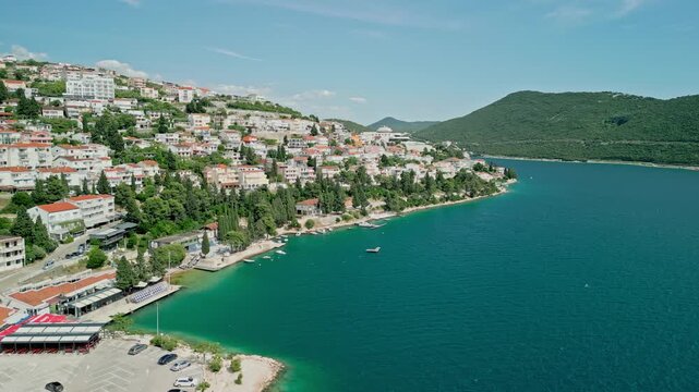 Neum, Bosnia and Herzegovina - 05 28 2025: Angled still drone video showing the Adriatic Sea on the right, mountains behind it, Neum coast with buildings and boats on the left, cars moving