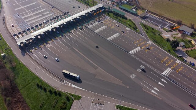 Drone aerial of highway toll booth lanes in northern Italy with vehicles passing through payment barriers. Transport infrastructure used for motorway traffic control and toll collection.