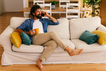 Obraz premium Happy man talking on smartphone while relaxing on sofa