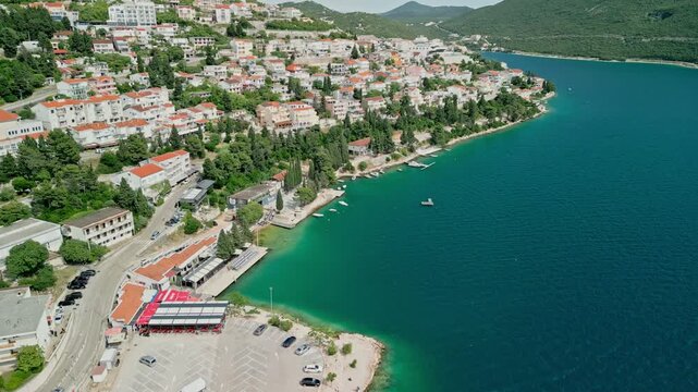 Neum, Bosnia and Herzegovina - 05 28 2025: Arc drone video showing the Adriatic Sea on the right, parking lot and residential buildings on the left, a street with moving cars, boats along the coast