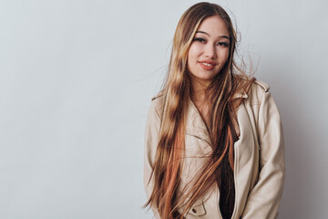 Obraz premium Young woman with long hair smiling in beige jacket standing against plain background casual fashion style confidence and beauty portrait indoors