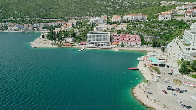 Neum, Bosnia Herzegovina - 05 28 2025: Arc drone video from down showing the Adriatic Sea on the left meeting Neum coast, with Neum beach, hotels, buildings along the coast and mountains in the back