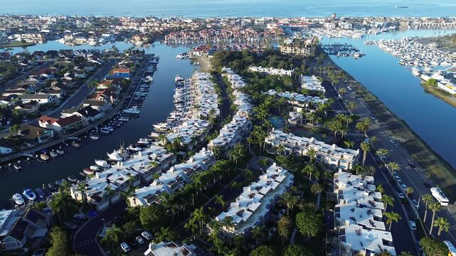 Wide basin view stretching toward outer Huntington Harbor marina near Anaheim Bay approach. Bright rooftops, townhouses, dense docks, layered coastal haze waterfront panorama, Huntington Beach, CA