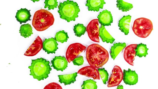 Animated motion footage displaying bright red tomato slices mixed with vibrant green bumpy bitter melon cross sections falling slowly video