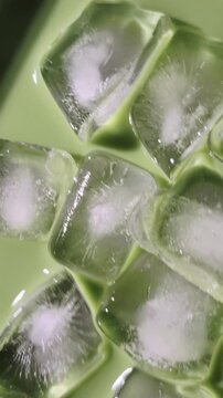 Macro view of ice cubes floating in green matcha latte or pistachio milk. Refreshing cold beverage texture. 4K vertical video.
