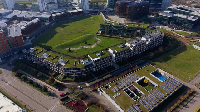 Aerial view showcases a vibrant green building complex seamlessly integrated into the cityscape, a testament to modern architectural brilliance, harmonious with nature.