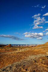 Wide desert landscape with layered sandstone rocks, distant mesas and dramatic blue sky with clouds in the American Southwest. Scenic wilderness panorama with vast open space.