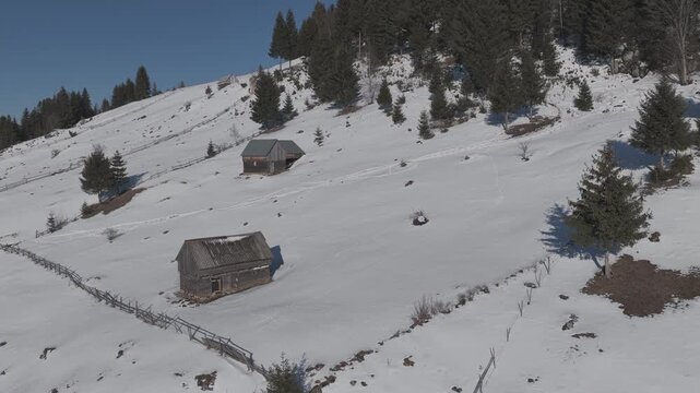 Fast ascending drone shot revealing rustic barns and the majestic snow-capped Bucegi Mountains in Moieciu de Sus, ungraded log