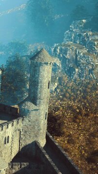 In a serene landscape, a towering castle stands proud against a backdrop of rocky cliffs and lush autumn trees. The soft mist adds a touch of mystery and enchantment.