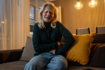 Young woman experiencing stomach pain sitting on sofa at home