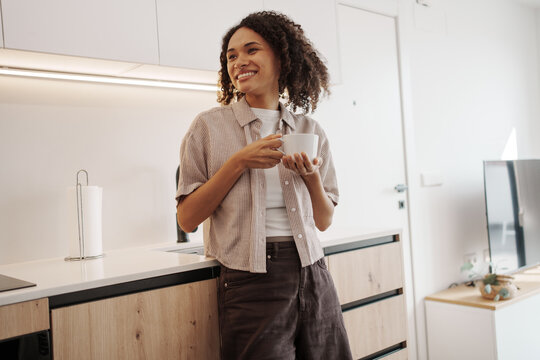 Female Expressing Happiness While Holding Mug In Comfortable Kitchen Environment With Bright Sunlight