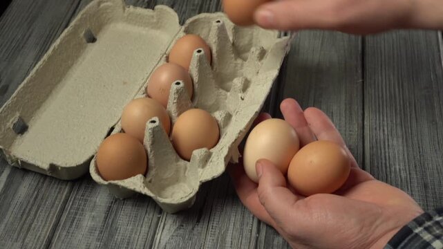 The hands of a man in a checkered shirt select and hold eggs from a carton, spreading them out on his hand, showing off the natural colors and texture of the egg
