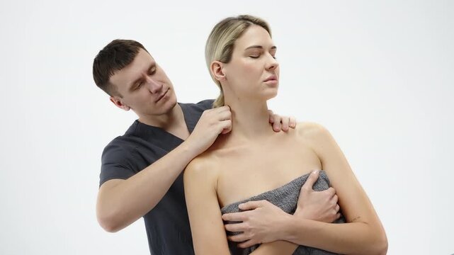 Professional neck and shoulder therapy session as a practitioner performs targeted cervical spine and trapezius massage on a towel-draped client in a clean, minimalist studio
