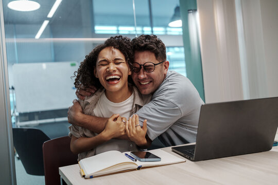 Happy Colleagues Share Warm Hug. Bright Office Scene Showcasing Genuine Emotion And Team Closeness