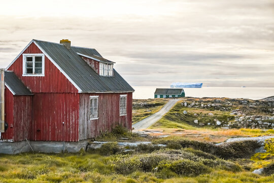 Qeqertarsuaq, Disko Island, Greenland - Seascape of Disko Bay coastline with charming seaside cottages, icebergs in the background under a moody sky