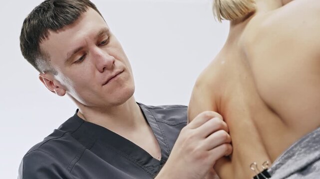 Physiotherapist performing manual palpation and assessment of a patient's upper back and shoulder, examining scapular muscles and tissue to evaluate tension and trigger points